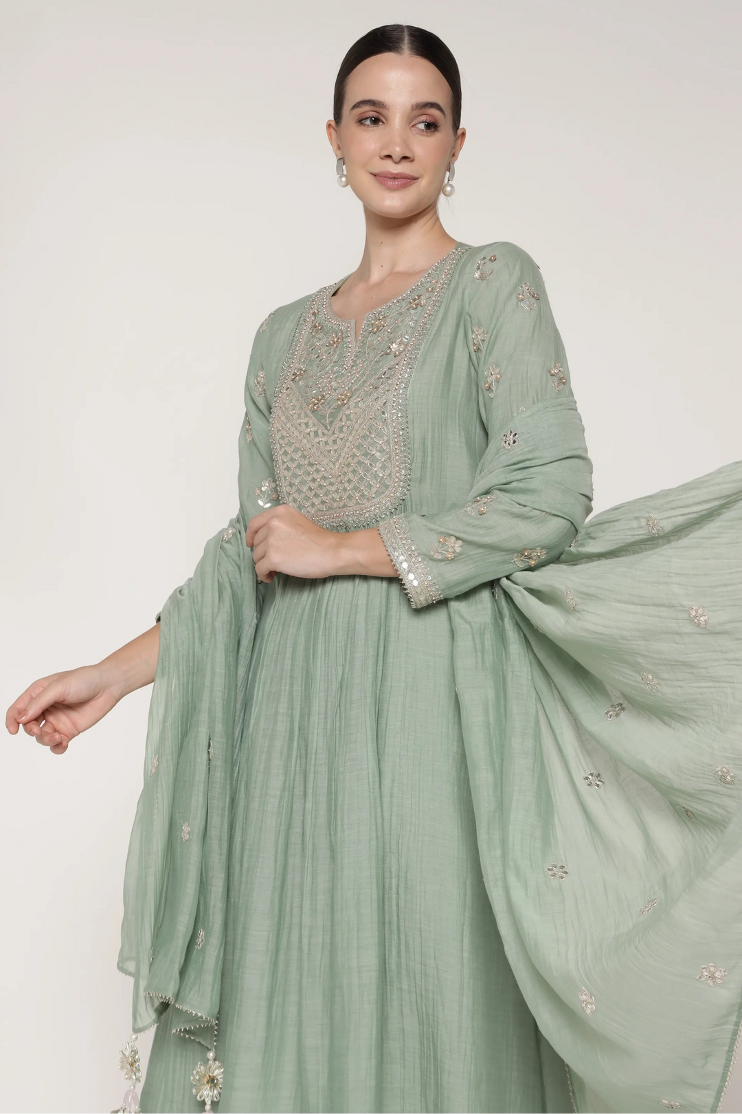 Woman wearing a light green traditional outfit with intricate detailing on a white background