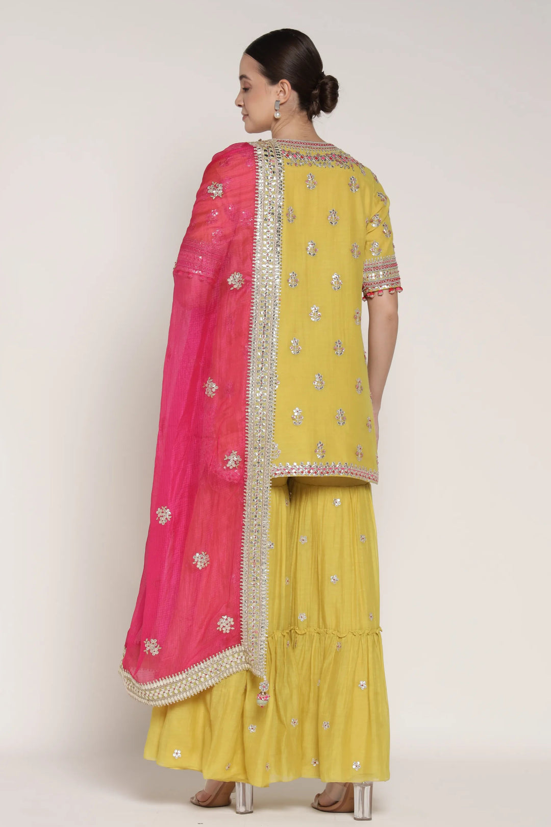 Woman wearing a yellow traditional outfit with a pink dupatta on a white background