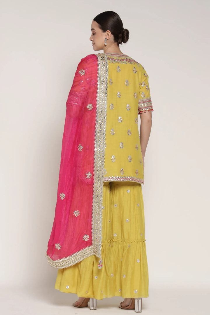Woman wearing a yellow traditional outfit with a pink dupatta on a white background