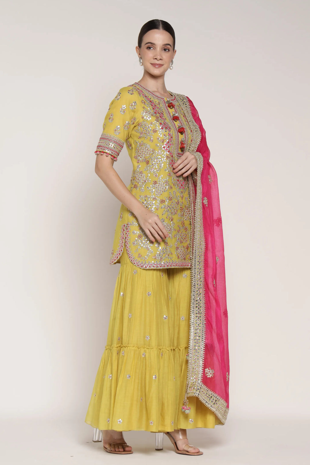 Woman wearing a yellow traditional outfit with pink dupatta on a white background