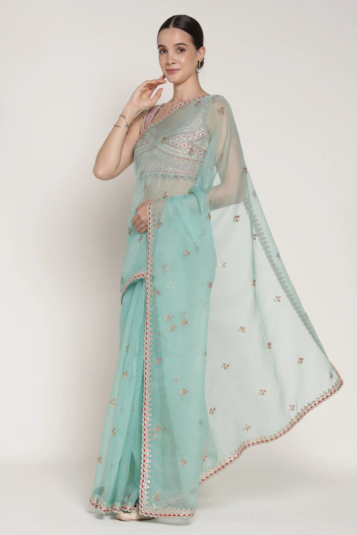 Woman wearing a light blue saree with a white blouse against a plain background