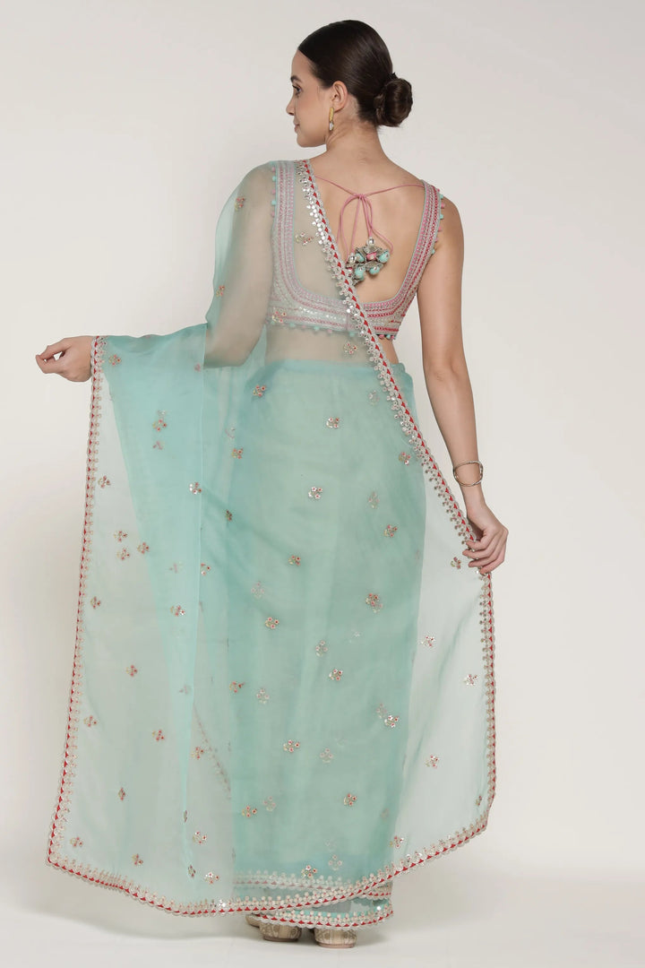 Woman wearing a light blue saree with a white blouse on a white background