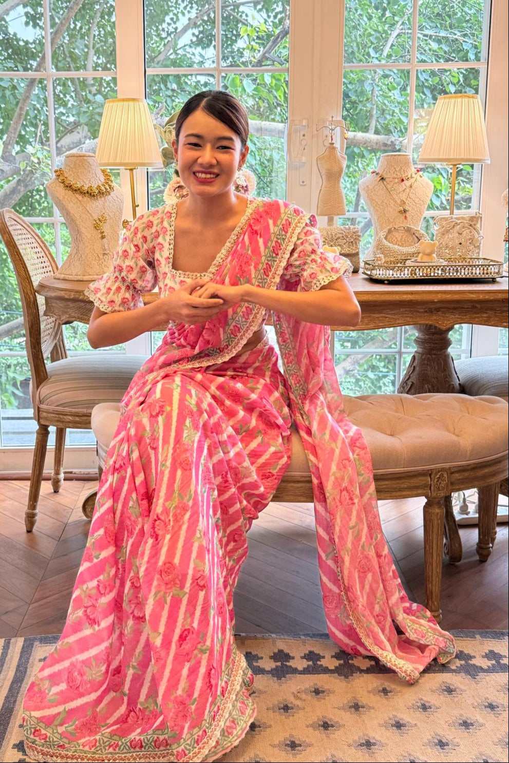 Woman in a pink outfit sitting on a chair in a room with large windows and decorative lamps.