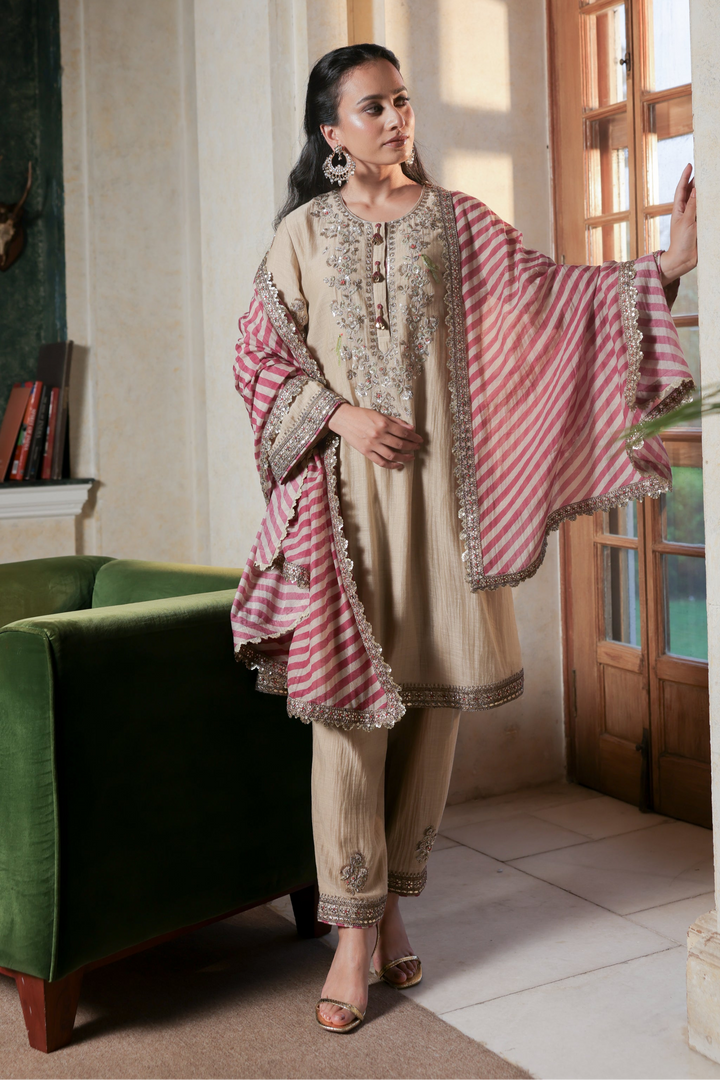Woman in traditional outfit standing in a room with a green armchair and decorative wall.
