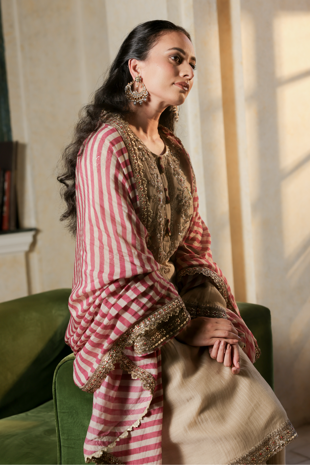 Woman in a pink and white striped outfit with gold accents sitting on a green chair.
