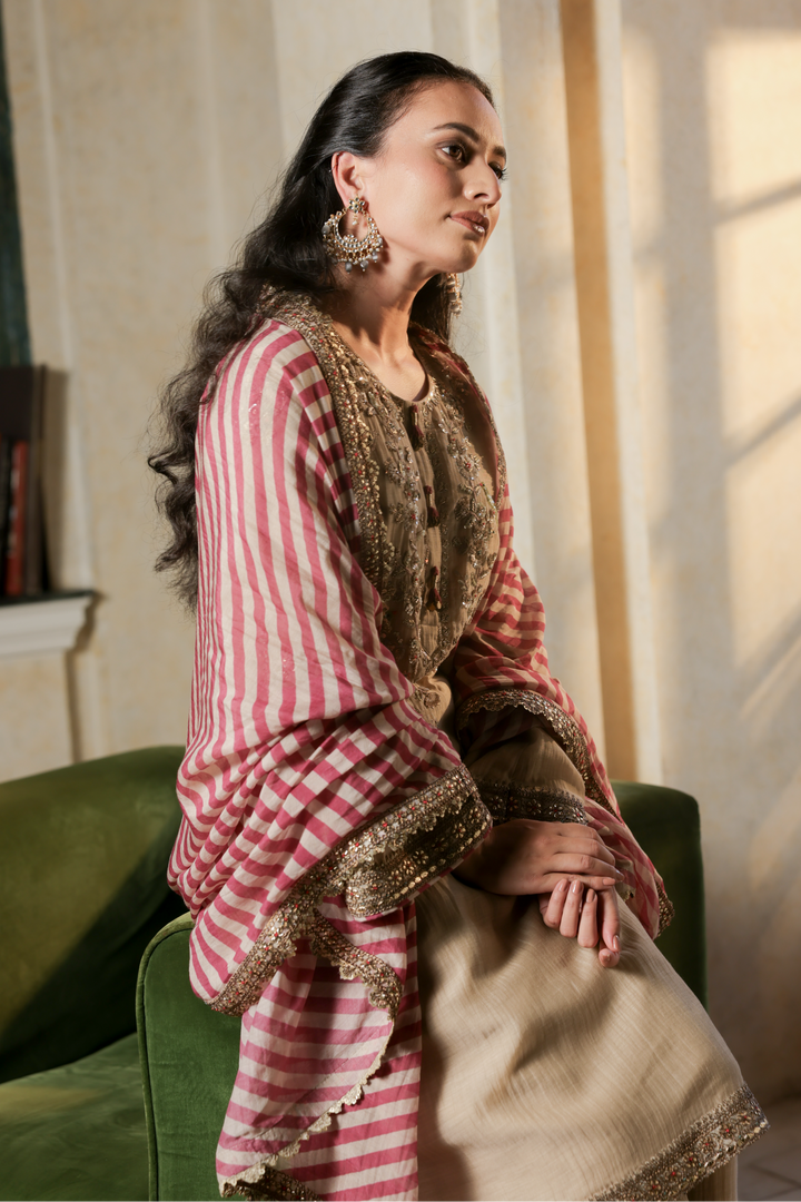 Woman in a pink and white striped outfit with gold accents sitting on a green chair.