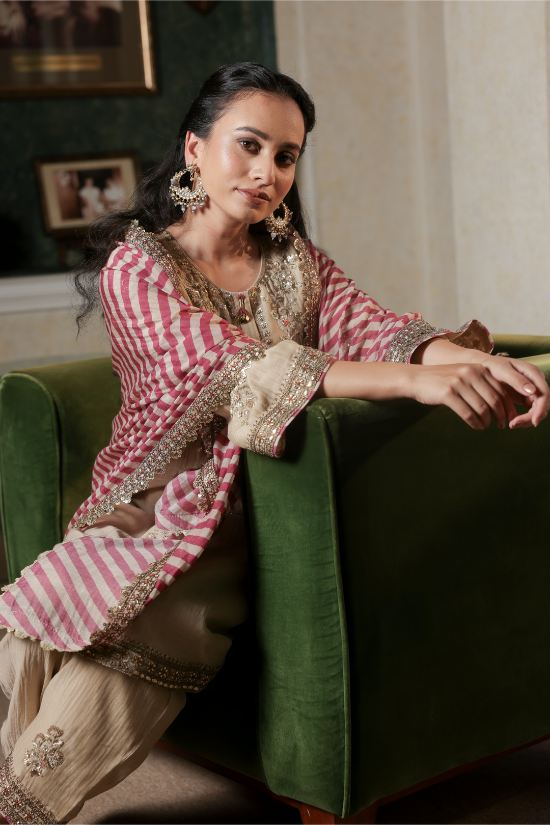 Woman in traditional outfit sitting on a green couch in an indoor setting