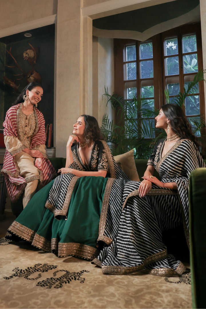 Three women in traditional attire sitting in a room with large windows.