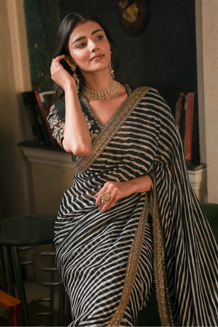 Woman in a black and white striped saree with gold border indoors.