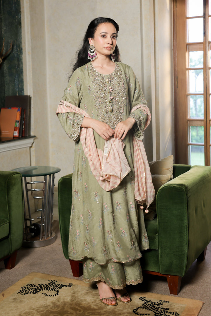 Woman in a green traditional outfit standing in a room with green furniture and a window.