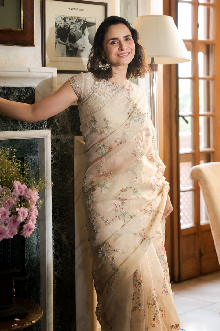 Woman in a floral saree standing in a room with decorative elements.