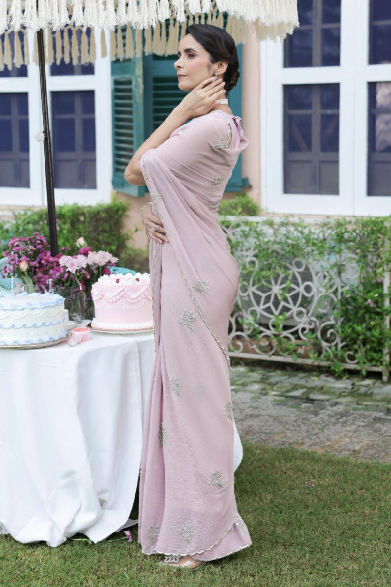 Woman in a pink saree standing outdoors with a decorated table in the background