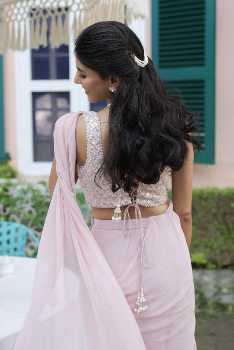Woman in a light pink traditional outfit with a long hair braid, standing outdoors.