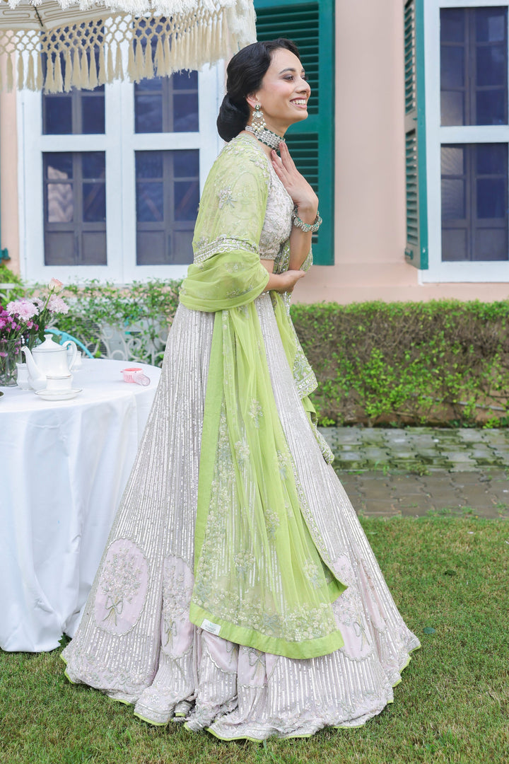 Woman in a light green and white traditional outfit standing outdoors with a table and umbrella in the background.