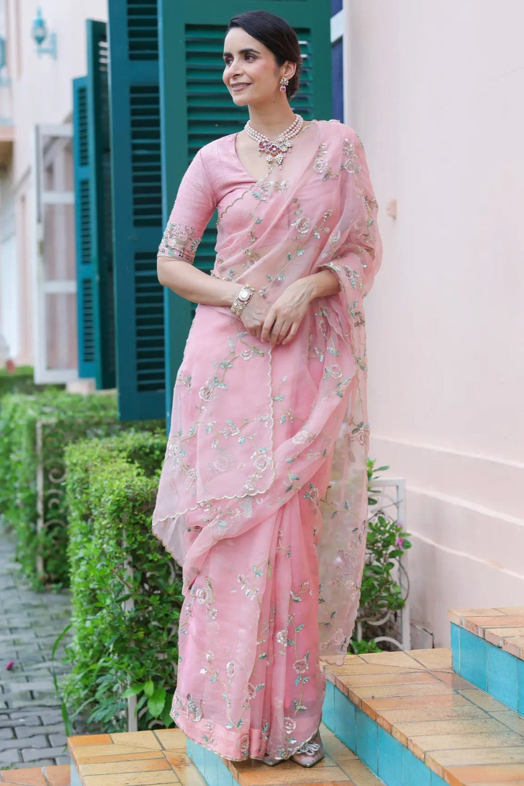 Woman in a pink saree standing on a wooden platform with a building in the background