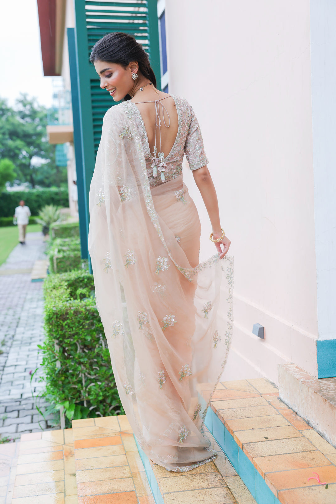 Woman in a beige saree with floral patterns standing outdoors.