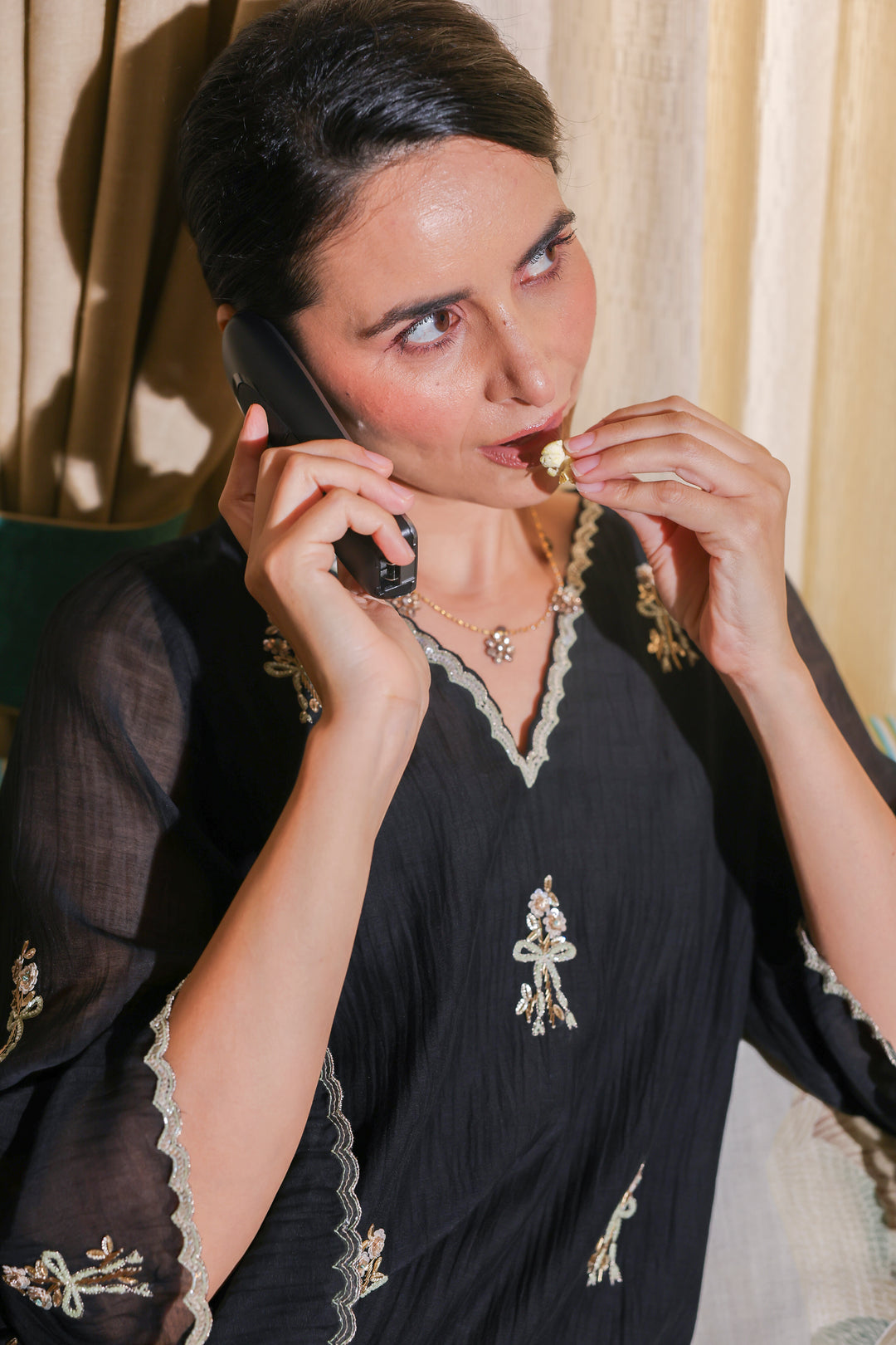 Woman in a black saree with gold embroidery talking on a phone.