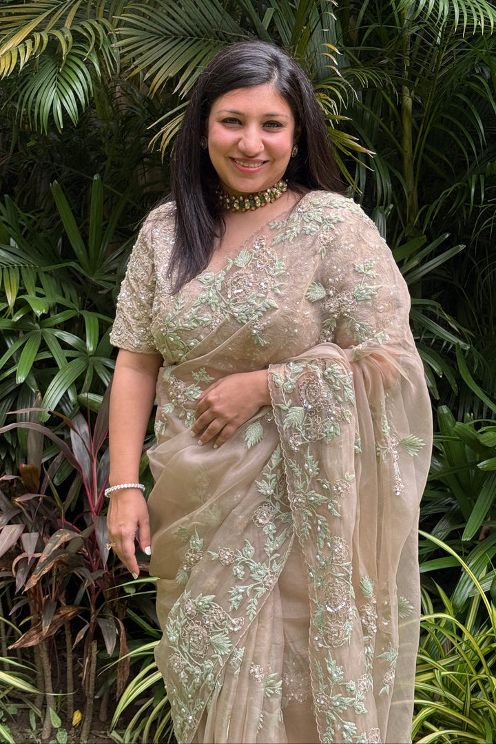 Woman in a beige saree standing among green plants