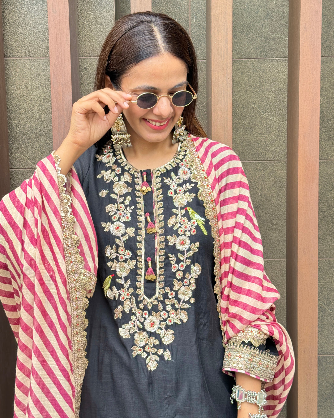 Woman wearing a traditional outfit with floral embroidery and a pink and white striped dupatta.