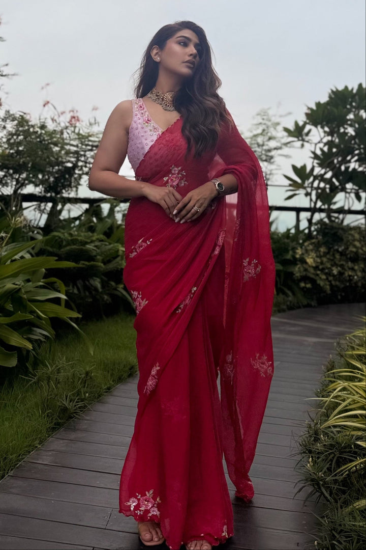 Woman in a red saree standing outdoors with greenery around