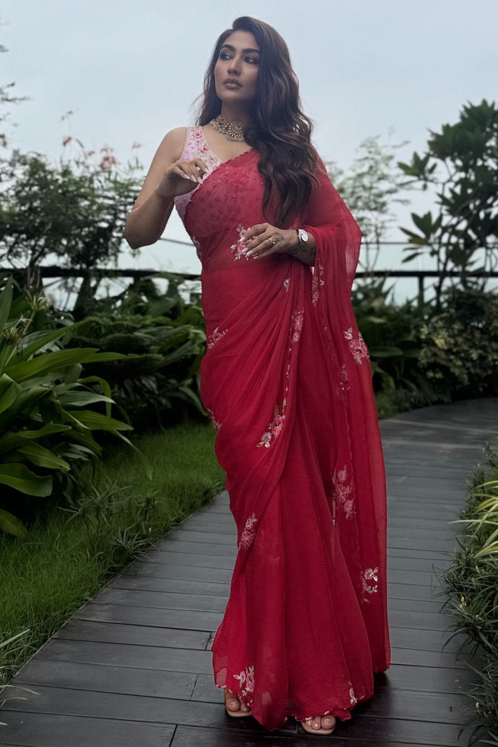 Woman in a red saree with white patterns walking on a garden path.
