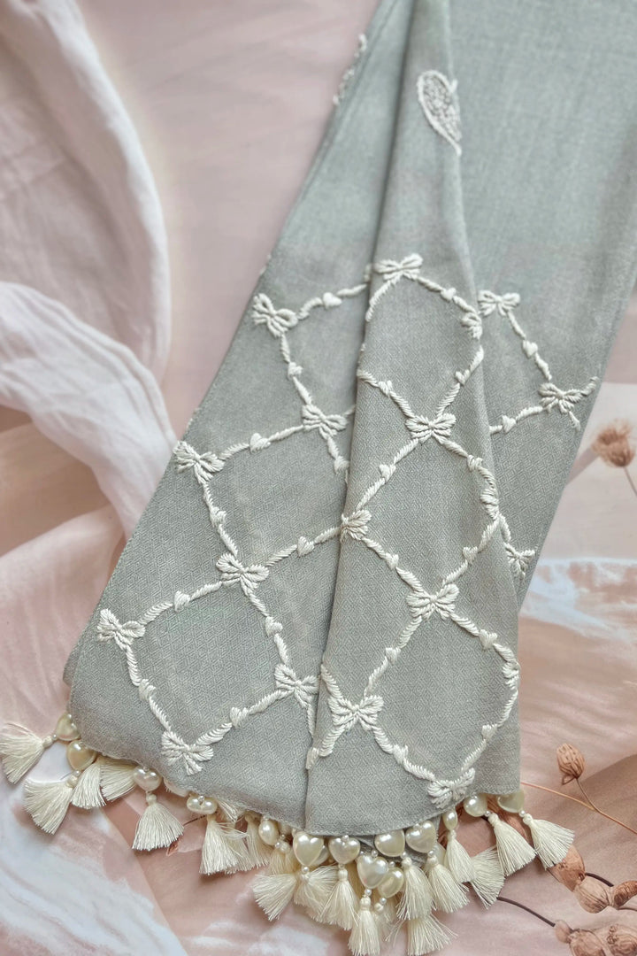 Gray towel with white lace and tassel details on a soft pink background