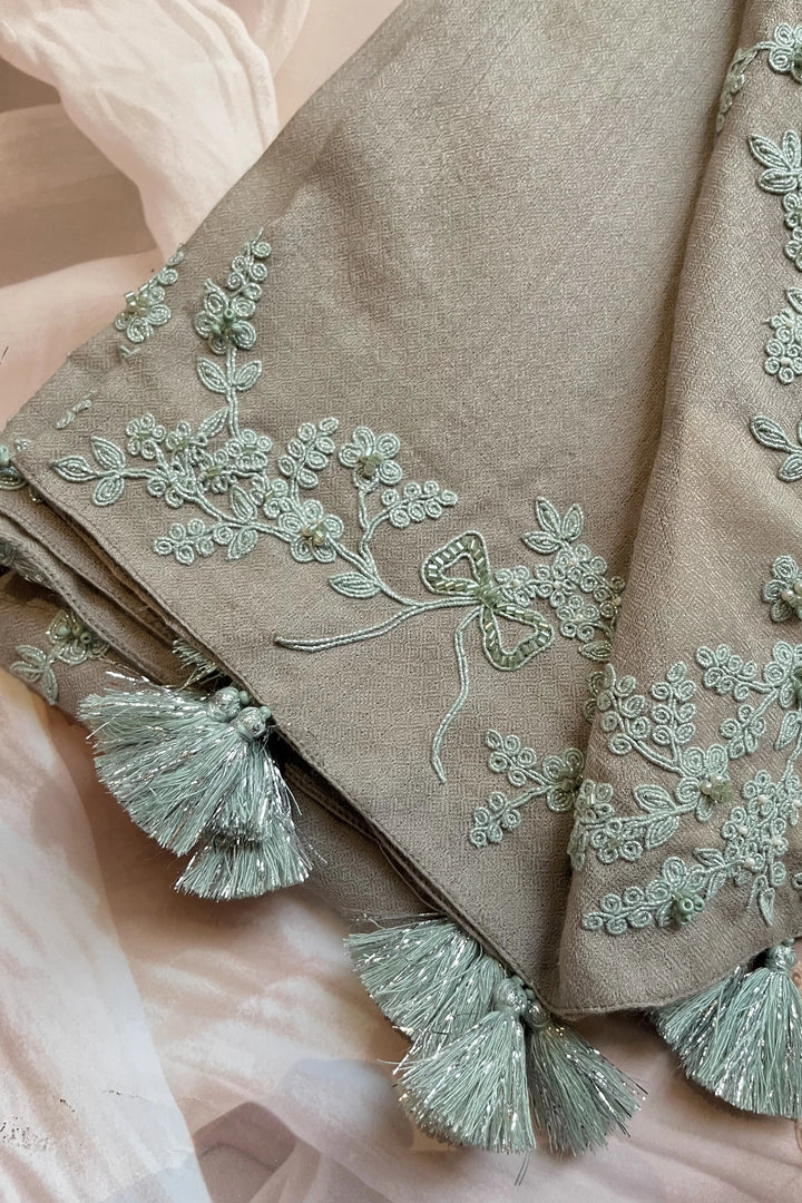 Brown fabric with intricate green embroidery and tassels on a soft pink background