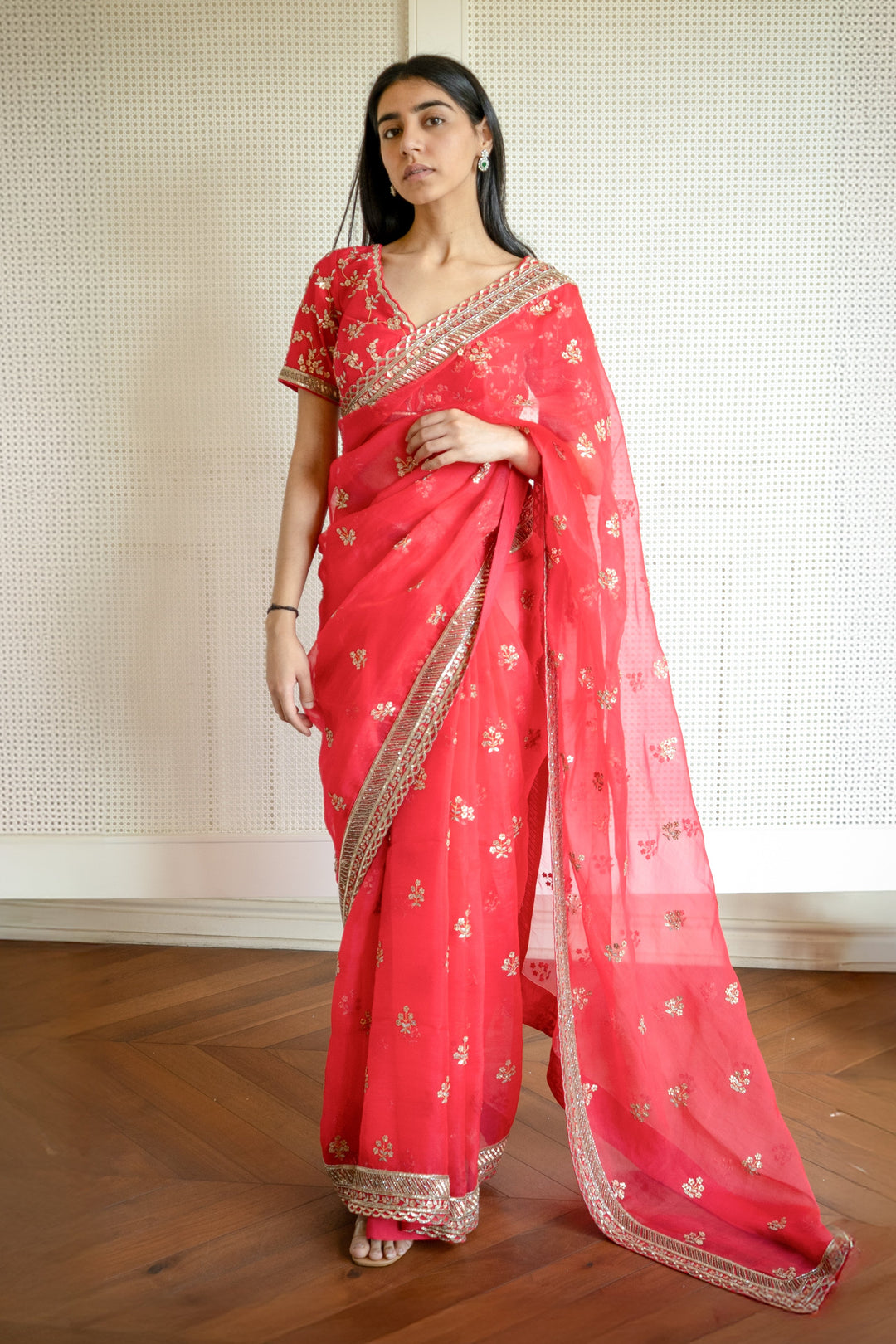 Woman wearing a red saree with gold patterns on a wooden floor.