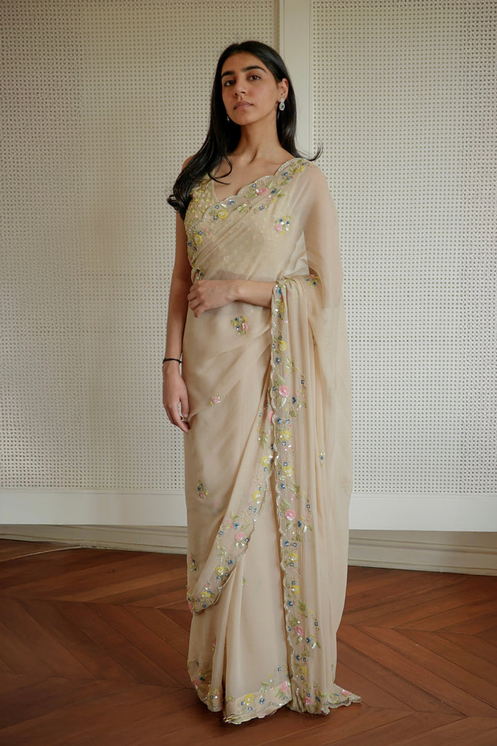 Woman wearing a beige saree with floral patterns against a neutral background