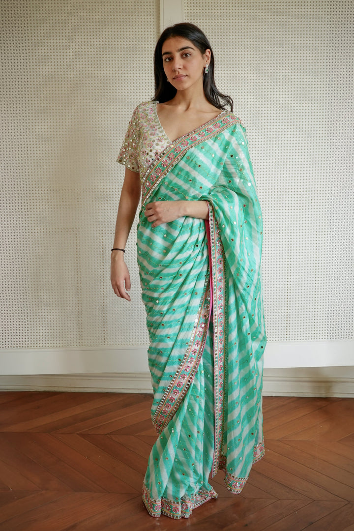 Woman wearing a green and white saree with a patterned border indoors.
