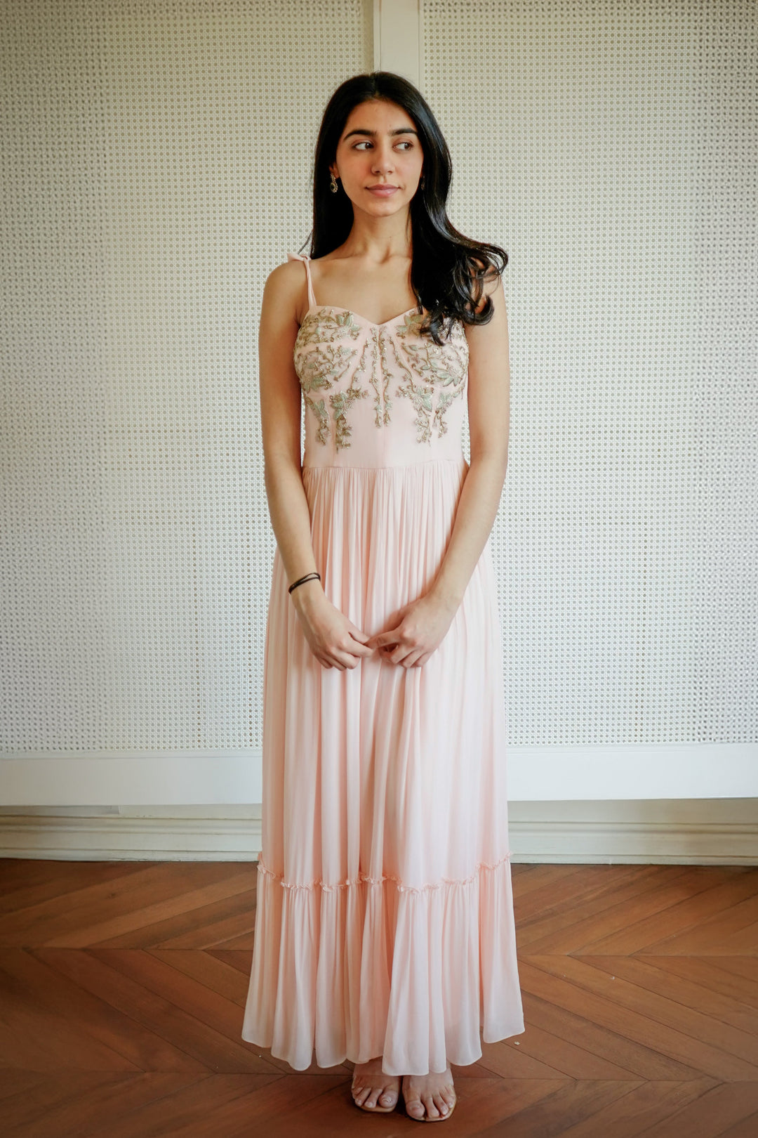 Woman in a long, light-colored dress standing against a textured wall.