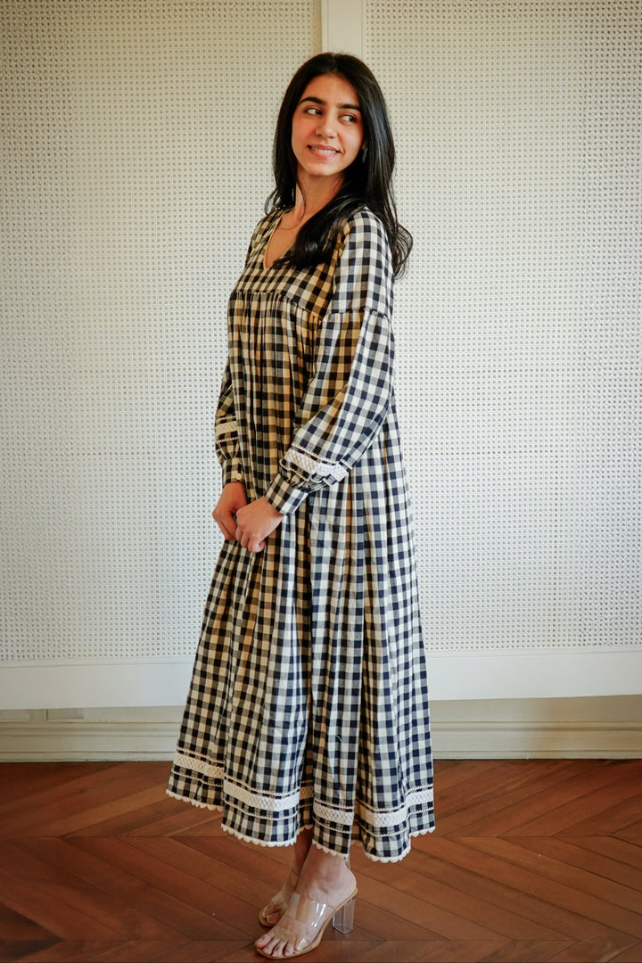 Woman wearing a checkered dress standing against a textured wall.