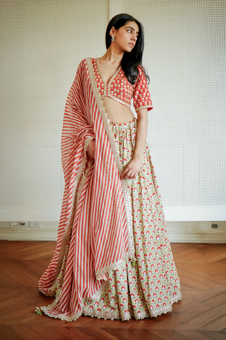 Woman wearing a red and white saree with a floral pattern on a wooden floor.