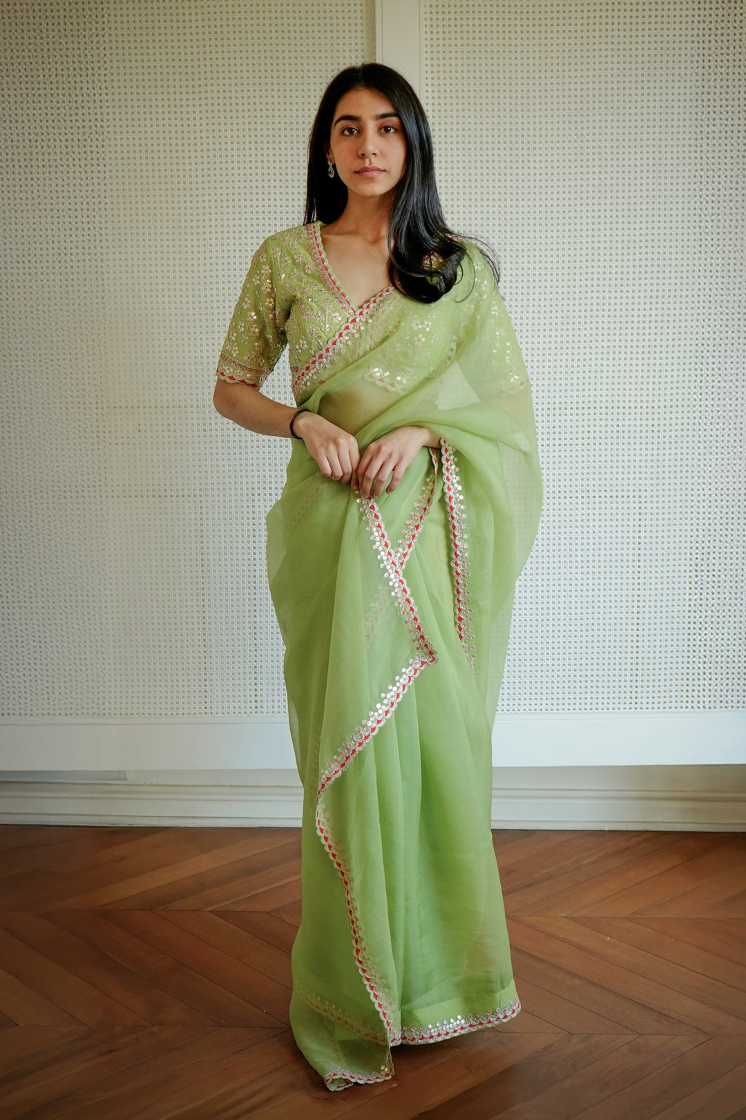 Woman wearing a light green saree with a white border indoors.