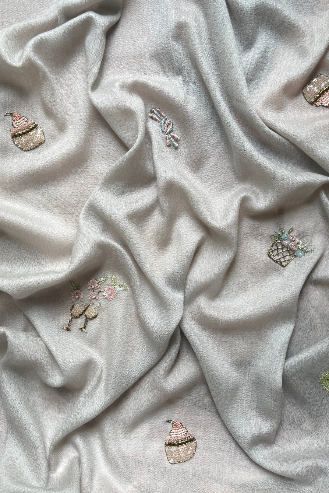 Light gray fabric with embroidered designs of cakes and flowers.