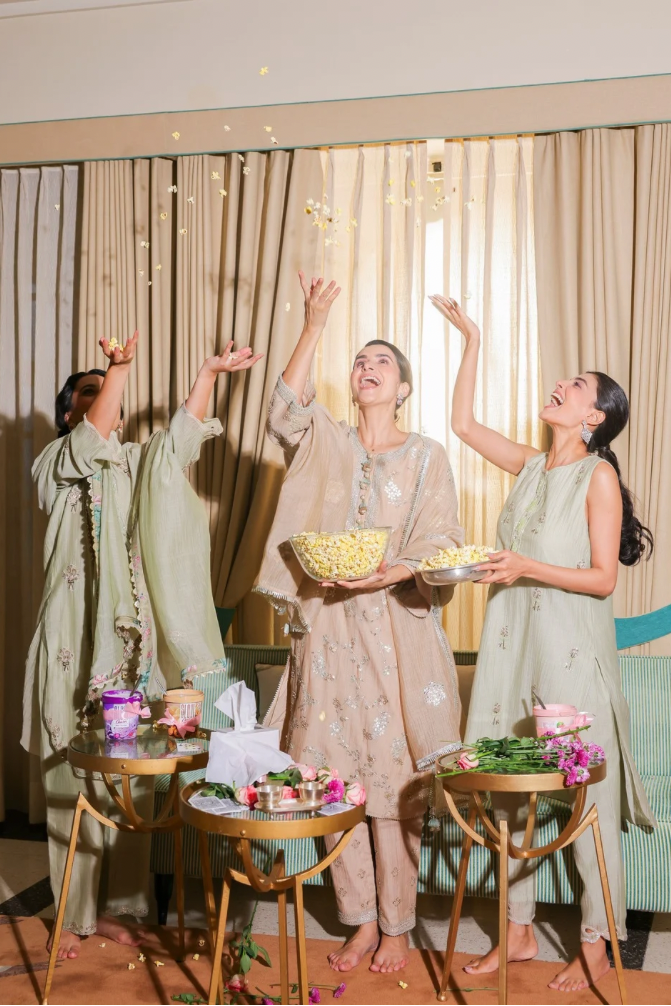 Three women in traditional outfits celebrating with bowls of snacks in a decorated room.