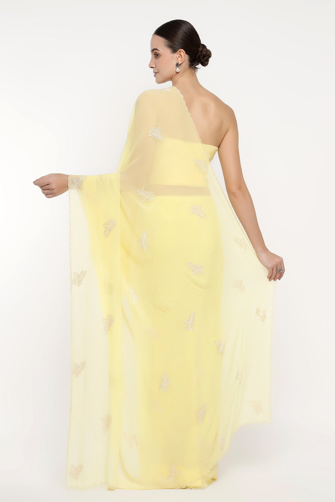 Woman wearing a light yellow one-shoulder dress with a sheer overlay on a white background