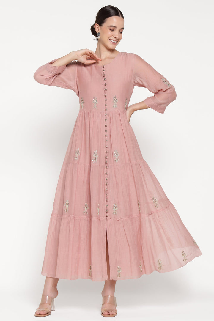 Woman wearing a pink dress with floral embroidery on a white background