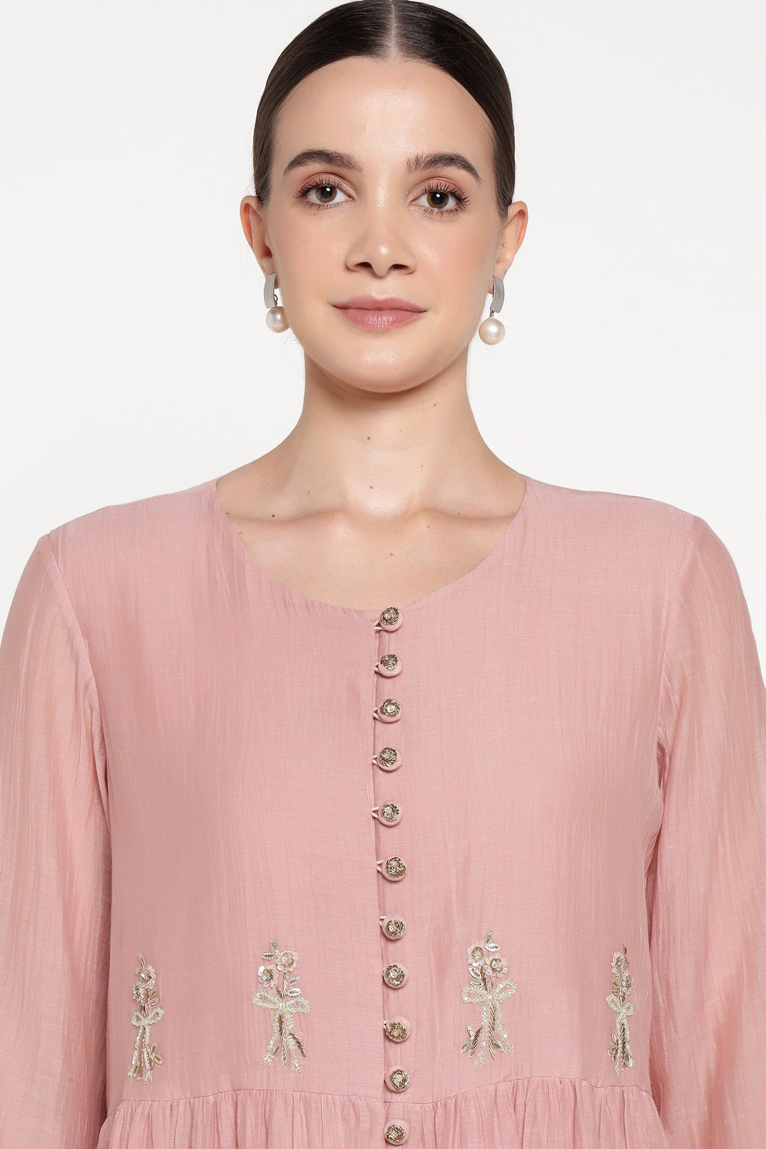 Woman wearing a pink dress with floral embellishments on a white background