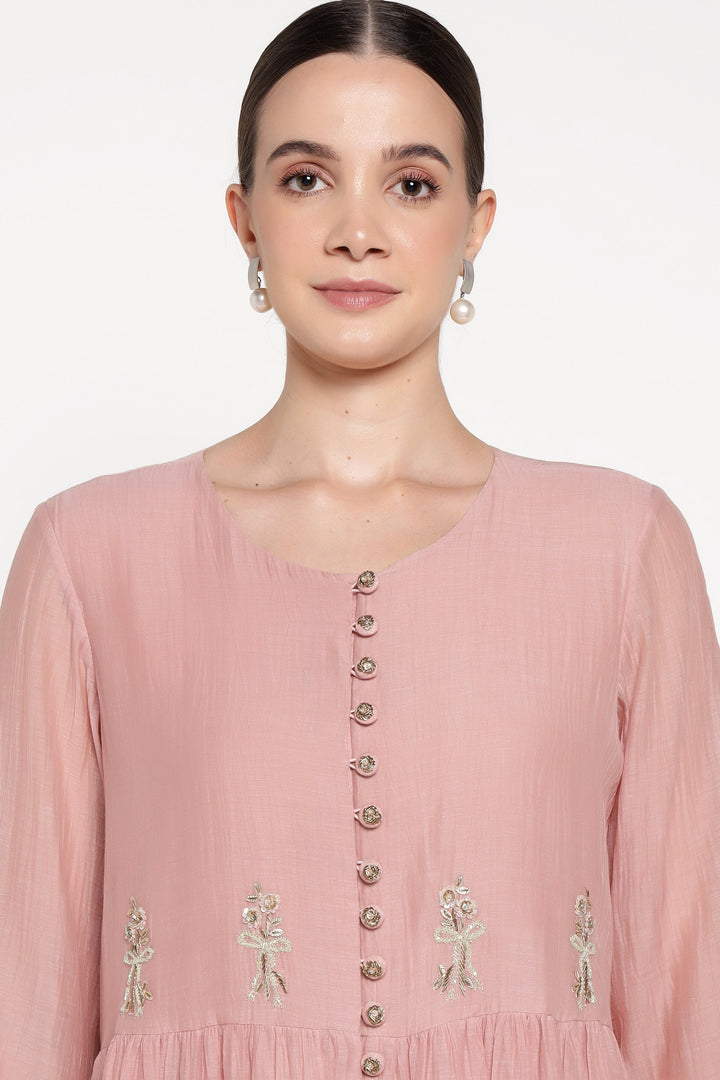 Woman wearing a pink dress with floral embellishments on a white background