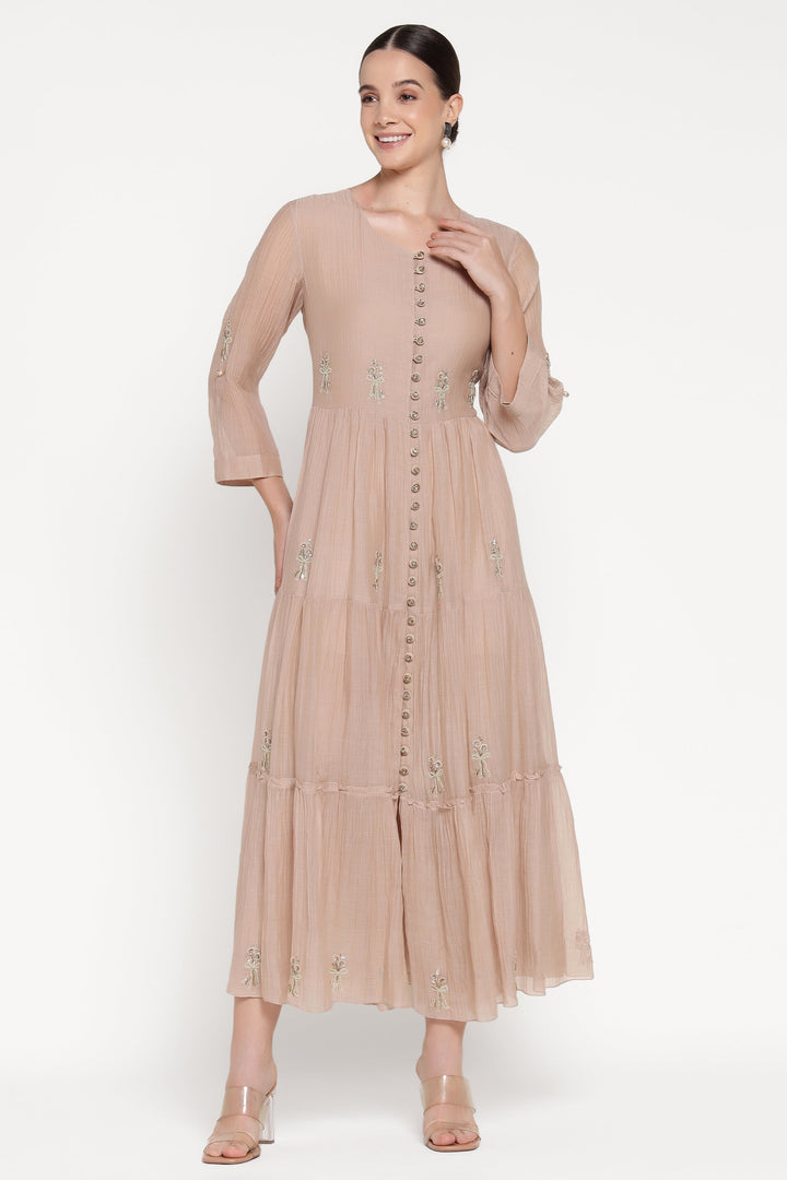 Woman wearing a beige dress with floral embellishments on a white background