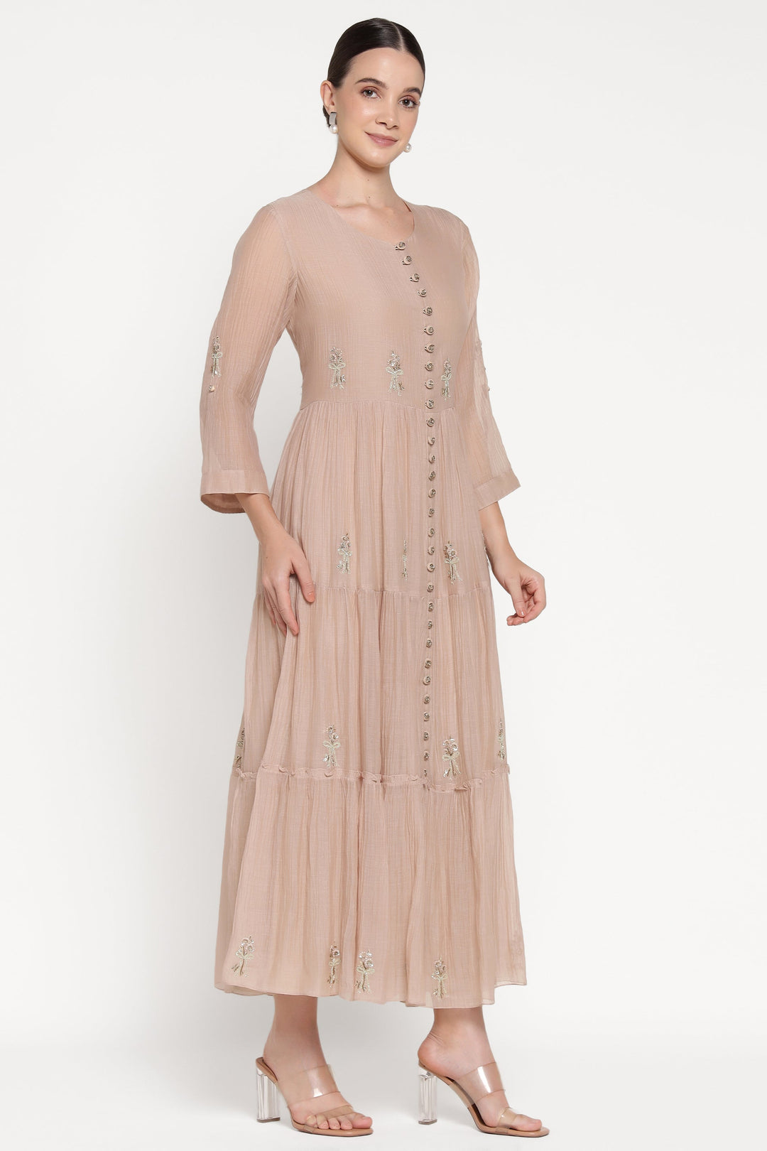 Woman wearing a beige dress with floral embellishments on a white background