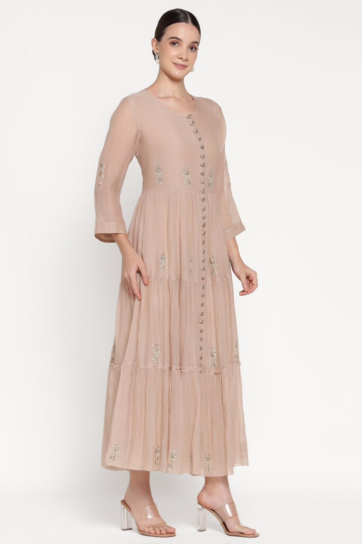 Woman wearing a beige dress with floral embellishments on a white background