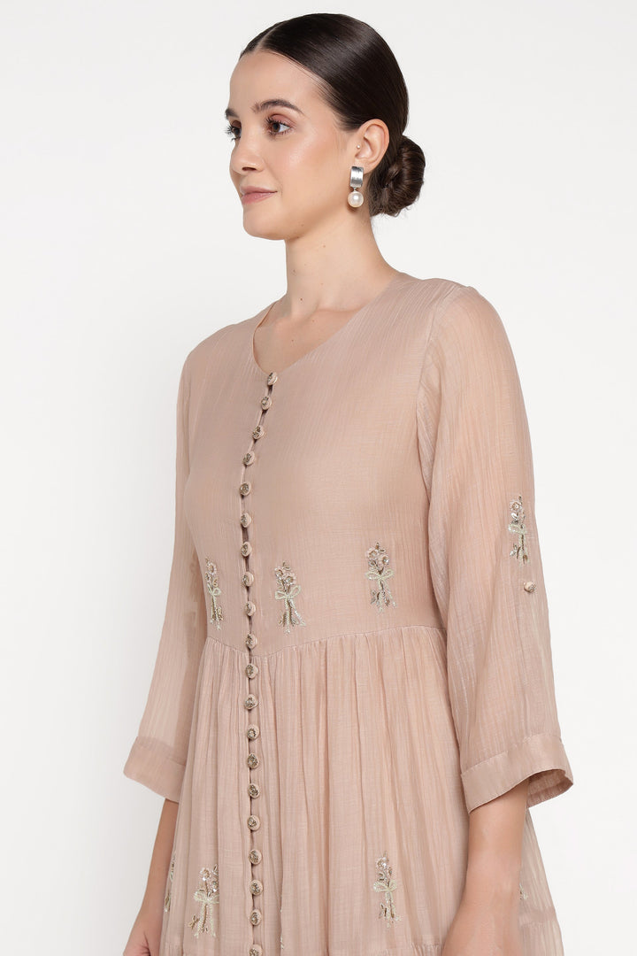 Woman wearing a beige dress with floral embroidery on a white background