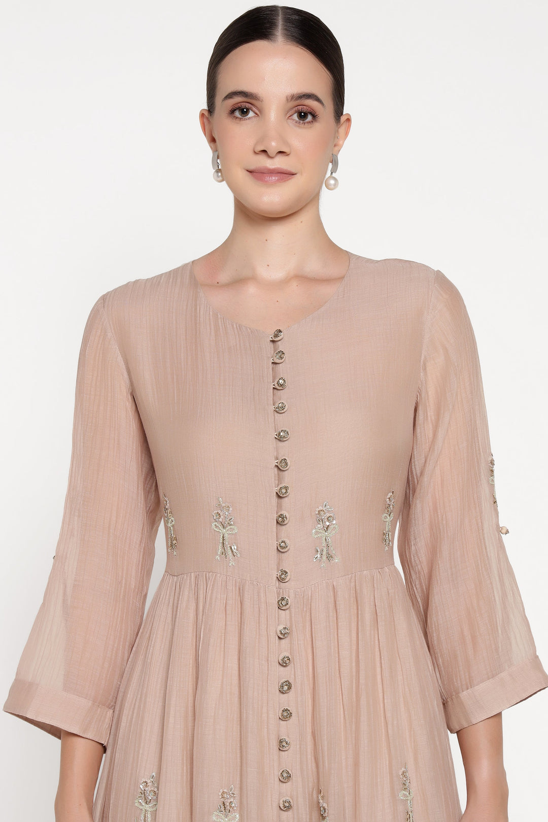 Woman wearing a beige dress with floral embroidery on a white background