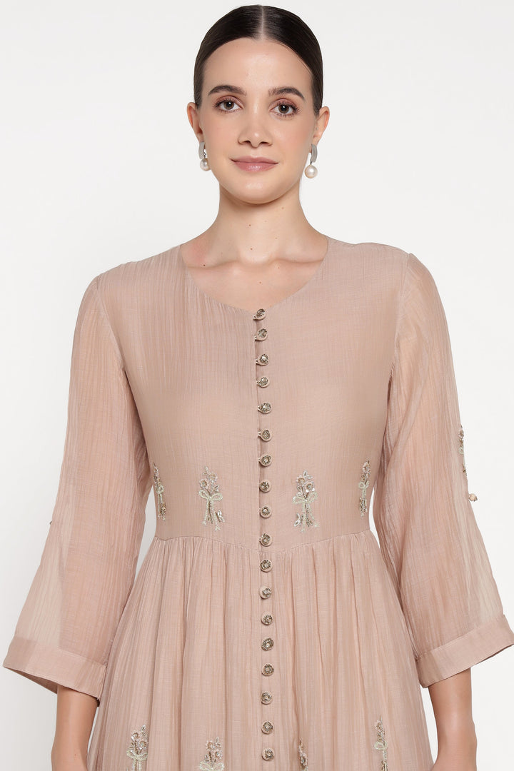 Woman wearing a beige dress with floral embroidery on a white background