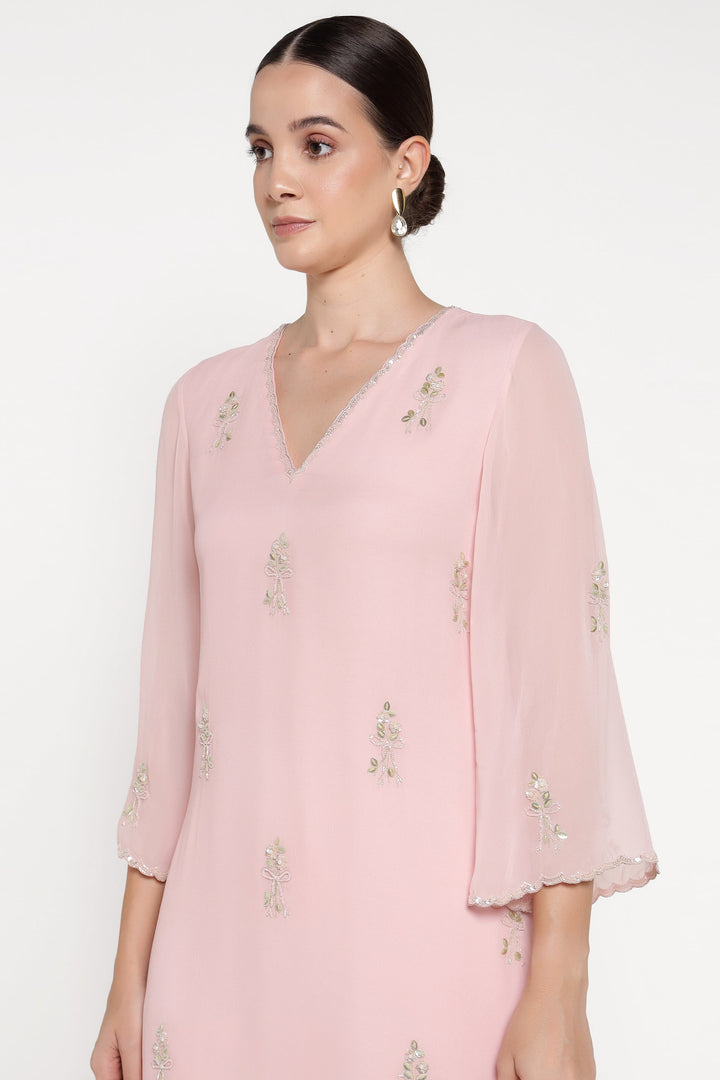 Woman wearing a light pink dress with floral embellishments on a white background