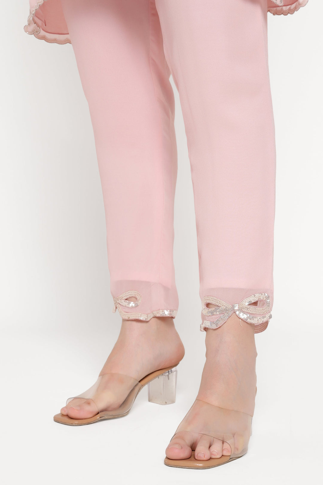 Pink pants with sheer bow accents and clear high-heeled sandals on a white background