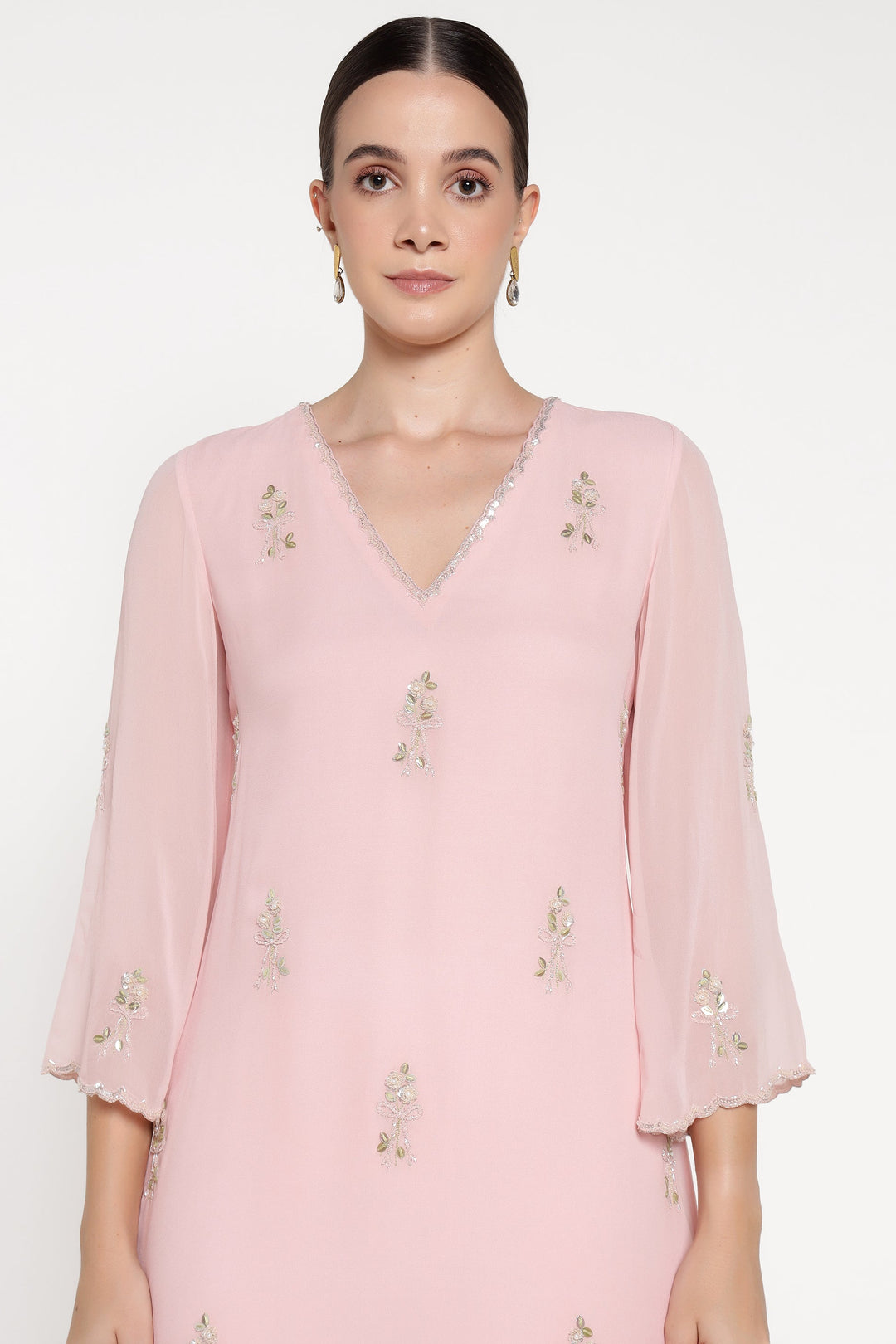 Woman wearing a light pink blouse with floral embroidery on a white background