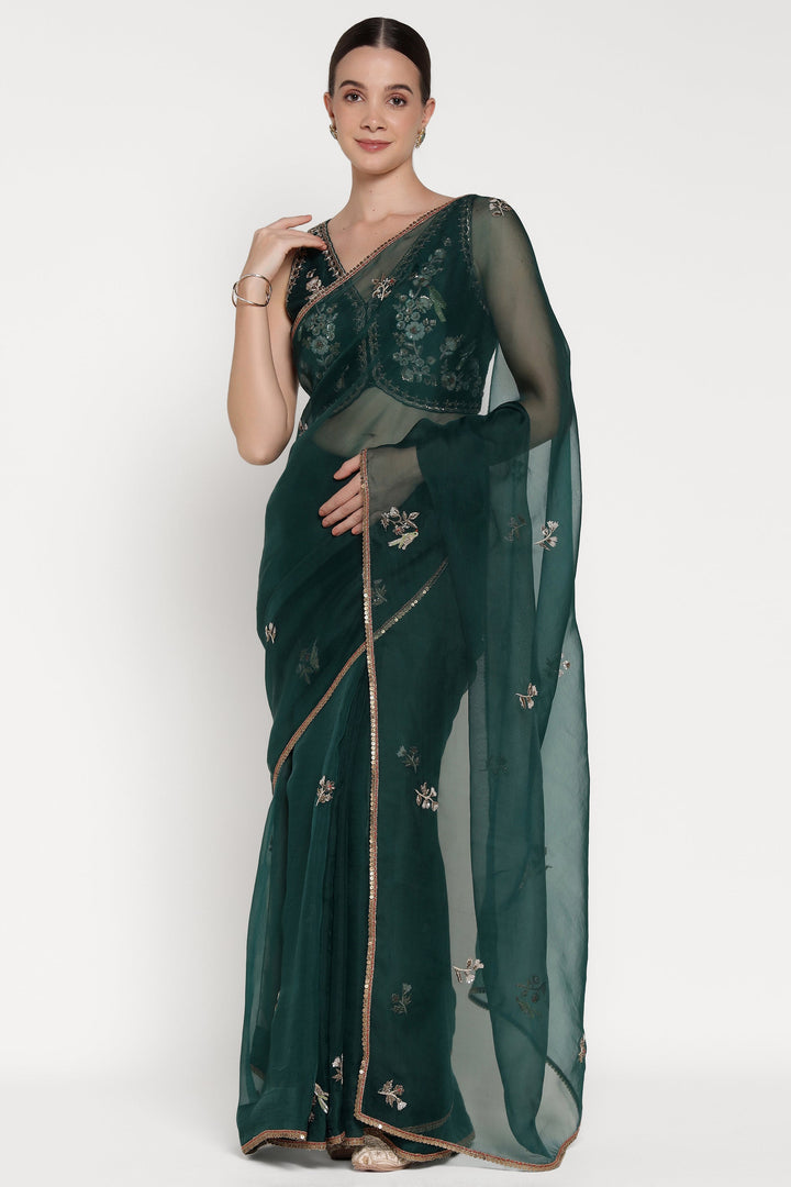 Woman wearing a dark green saree with floral patterns on a white background